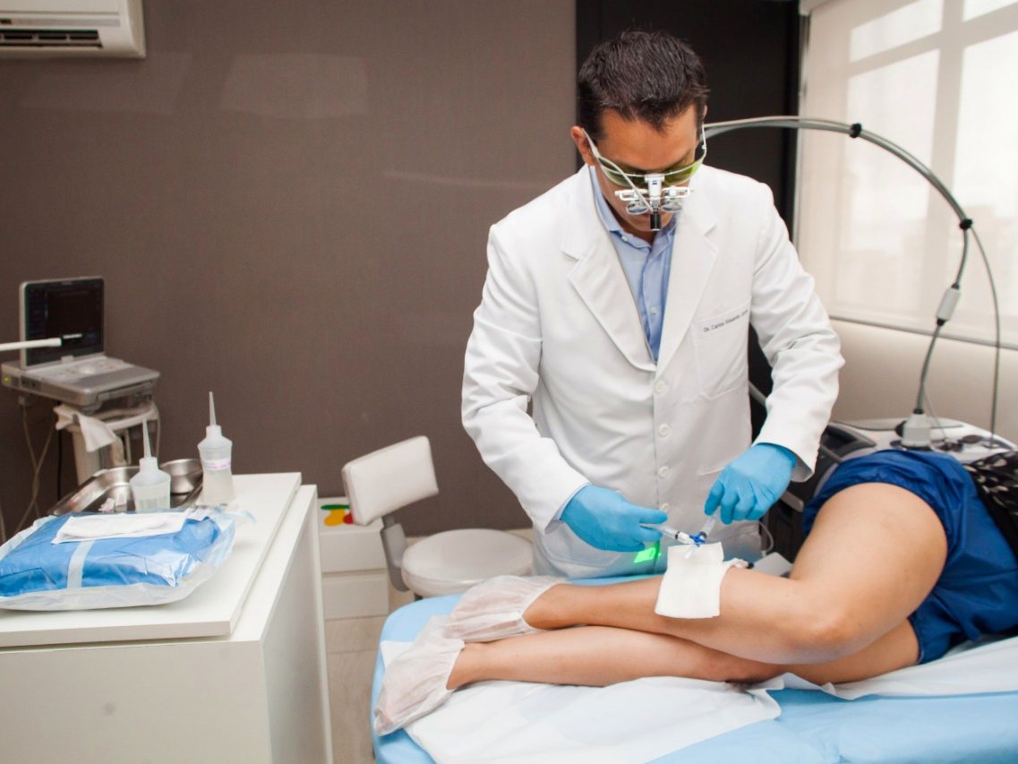 Dr. Cadu aplicando escleroterapia guiada pelo mapa verde projetado na perna
