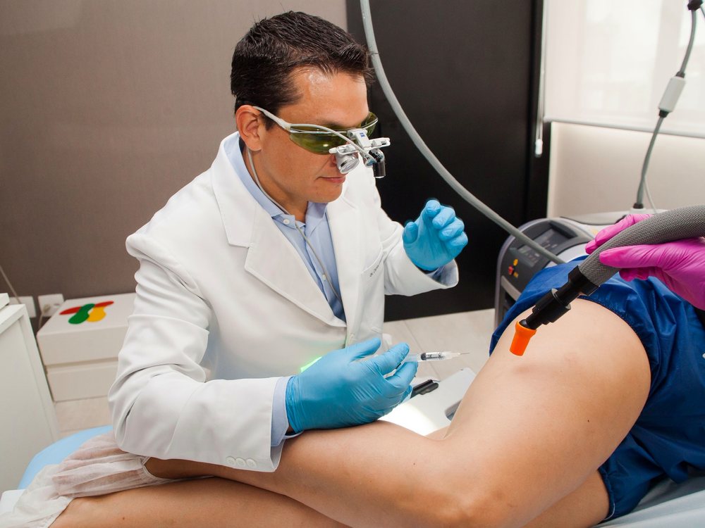Dr. Cadu com lupa cirúrgica e óculos de proteção durante aplicação de laser na perna