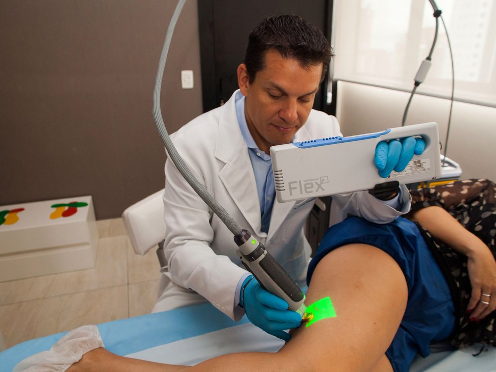 Dr. Cadu segurando o VeinViewer Flex e aplicando o laser sobre o mapa projetado